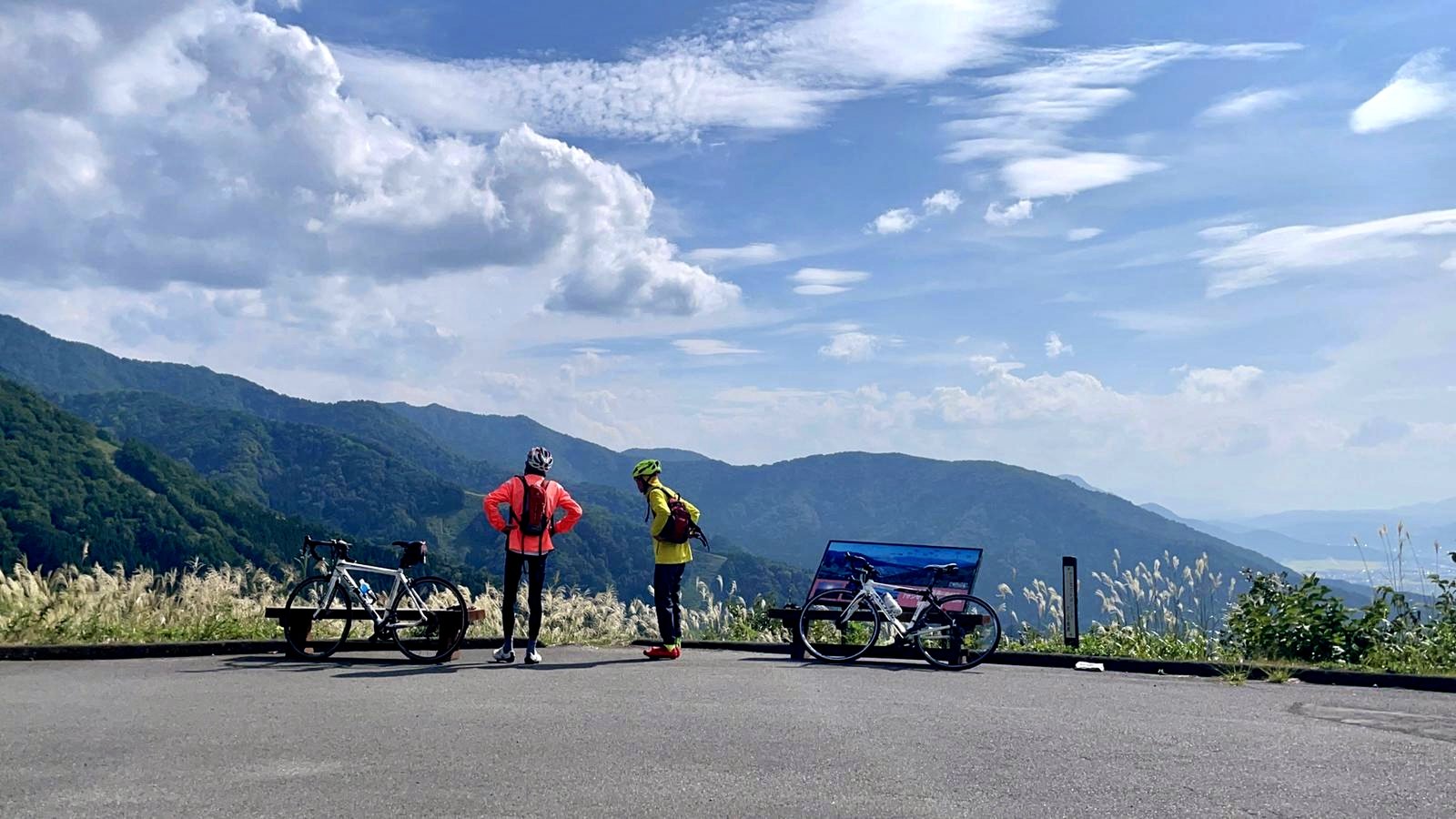 Two people with their bikes standing on a mountain side, with a majestic mountain range in the background.