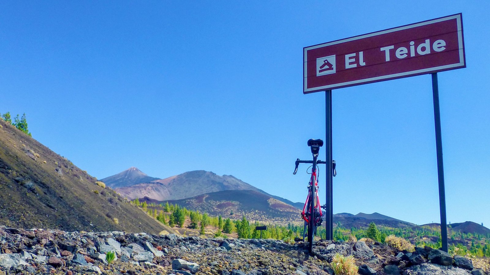 bicycle leaning on a sign indicating “El Teide” with the mountain in the background