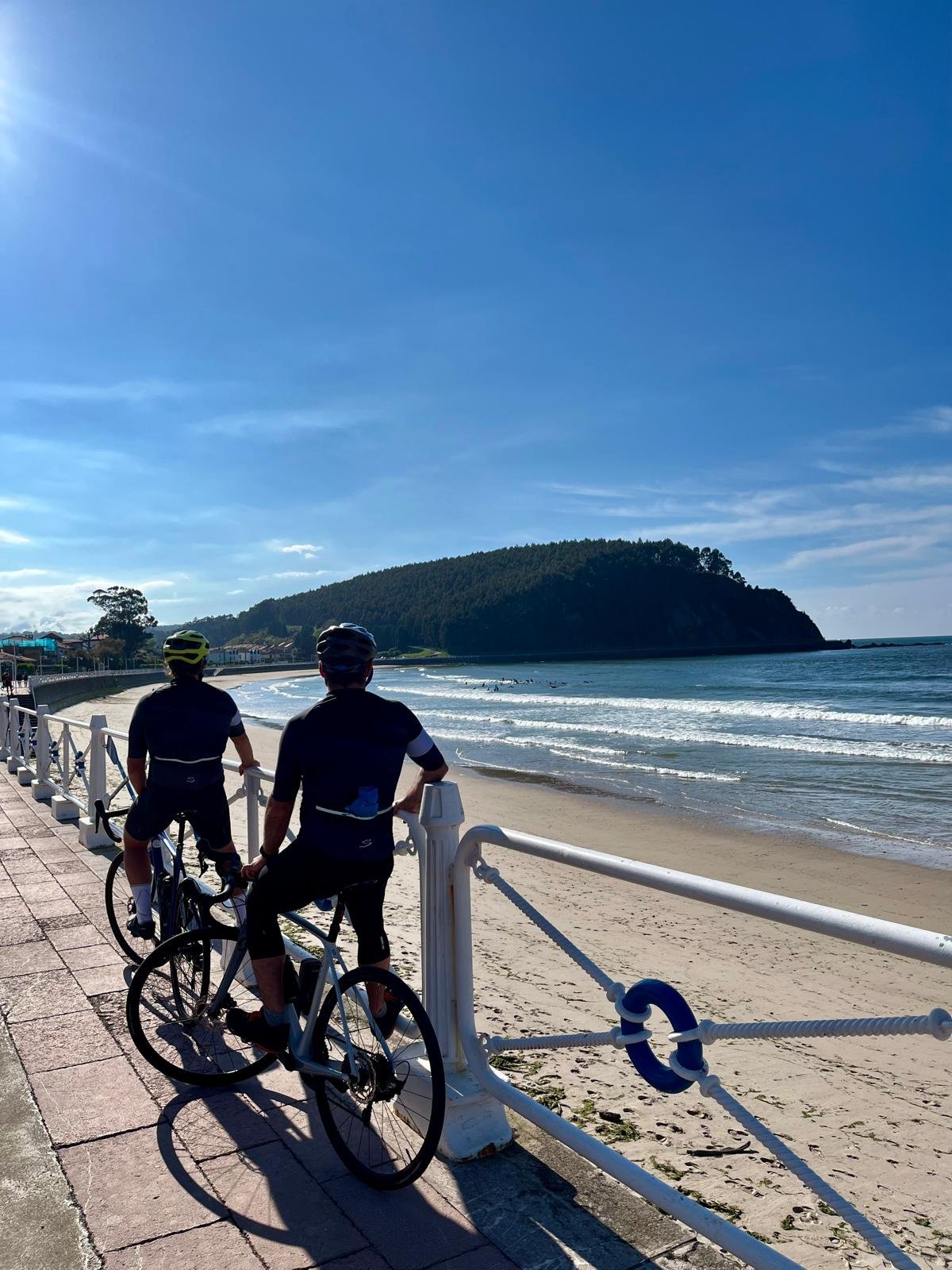 Two people riding bikes on the beach with the Mediterranean sea in the background.